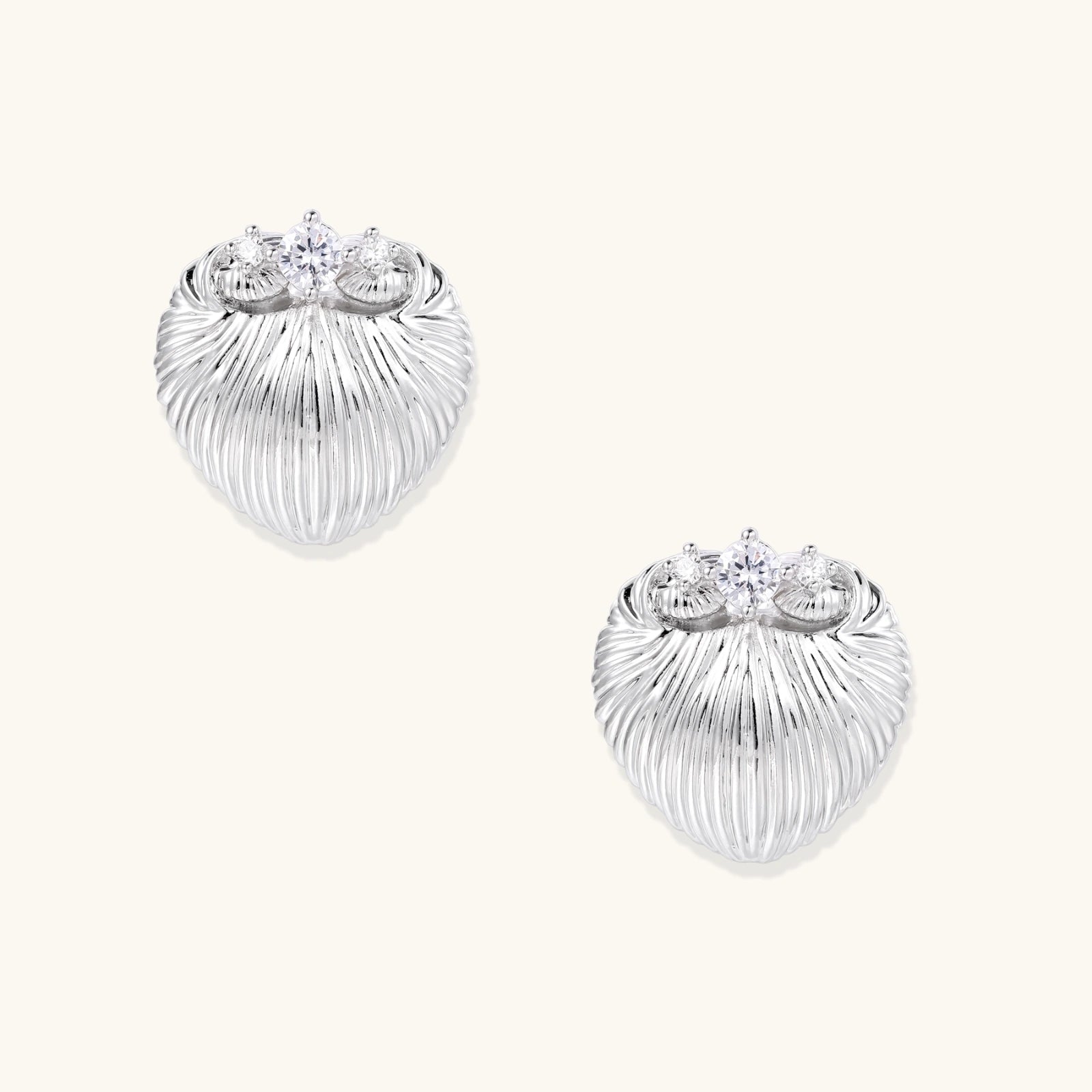 White gold-plated shell-textured stud earrings with three zirconia crystals on ridged surface against cream background.