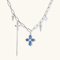 White gold plated chain necklace with blue textured cross pendant, spike charms, and mini cross detail on beige background