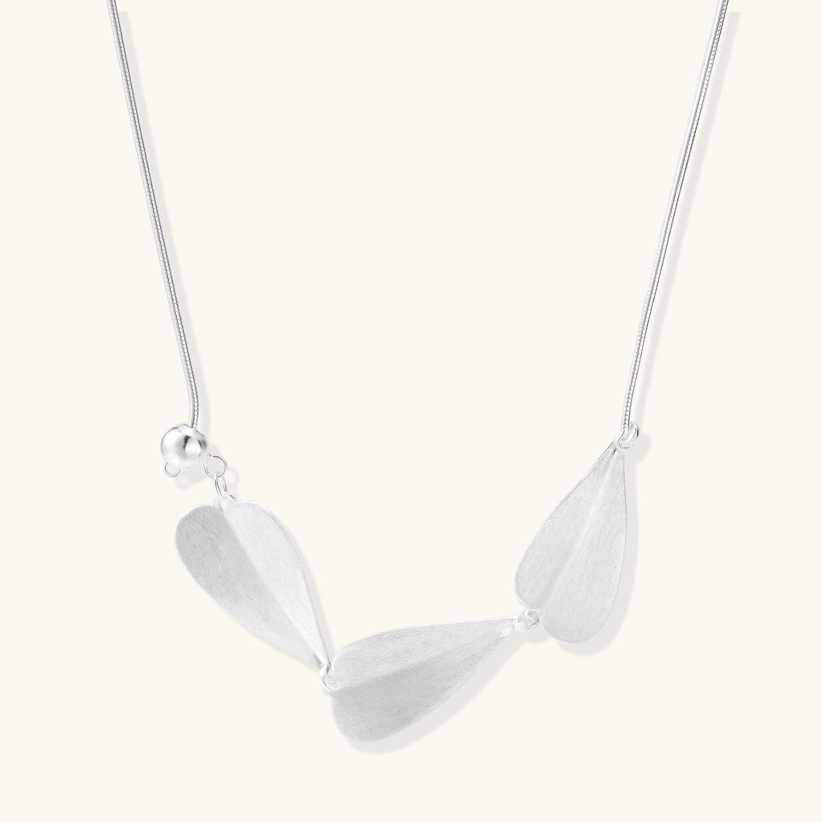 Minimalist sterling silver necklace with three brushed leaf-shaped pendants on delicate chain against white background