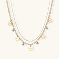 Gold layered necklace set with engraved heart pendants and crystal accents on cream background