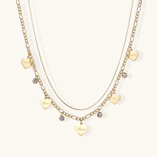 Gold layered necklace set with engraved heart pendants and crystal accents on cream background