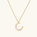 Gold crescent moon pendant with graduated white pearls on delicate chain against cream background