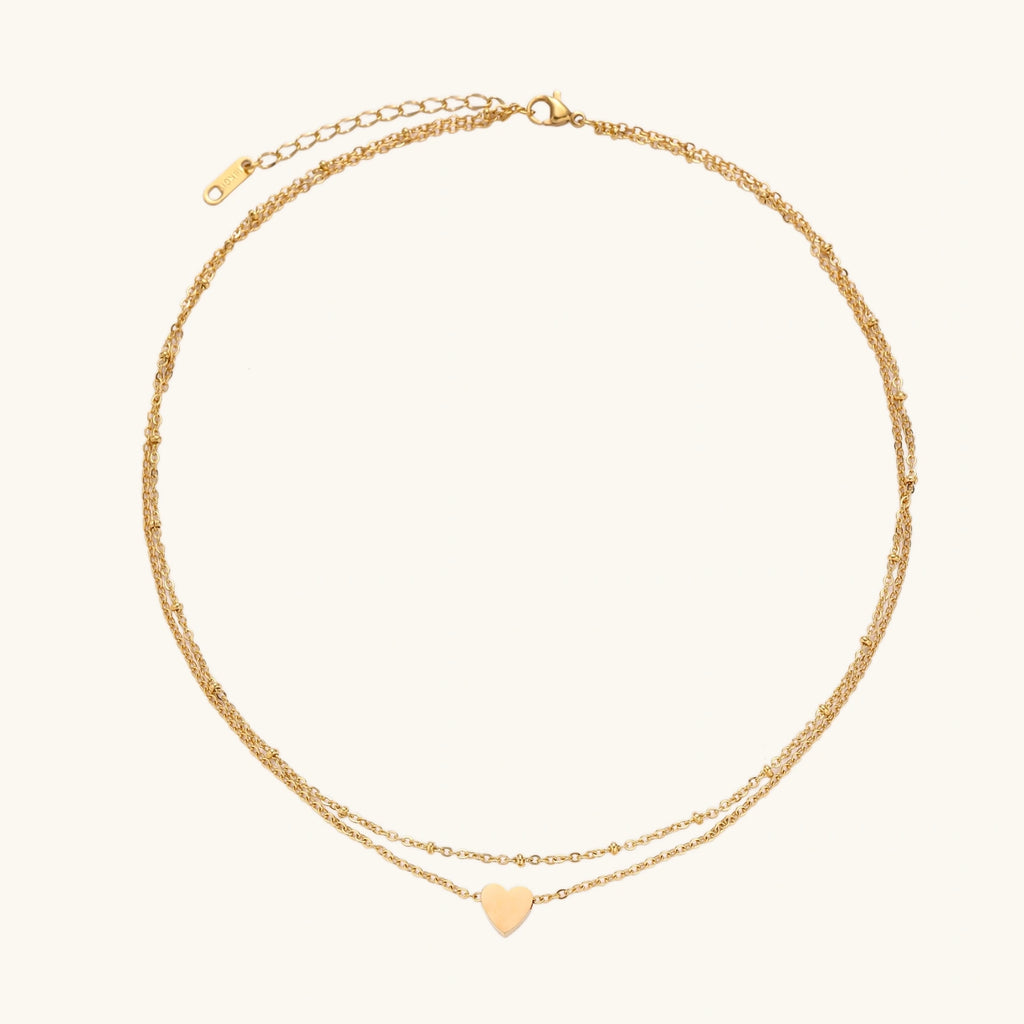 Delicate double-chain gold necklace with tiny heart pendant on cream background