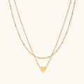 Delicate double-chain gold necklace with tiny heart pendant on cream background