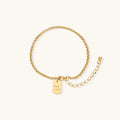Delicate 18K gold-plated chain bracelet with Good Luck engraved rectangular pendant on cream background