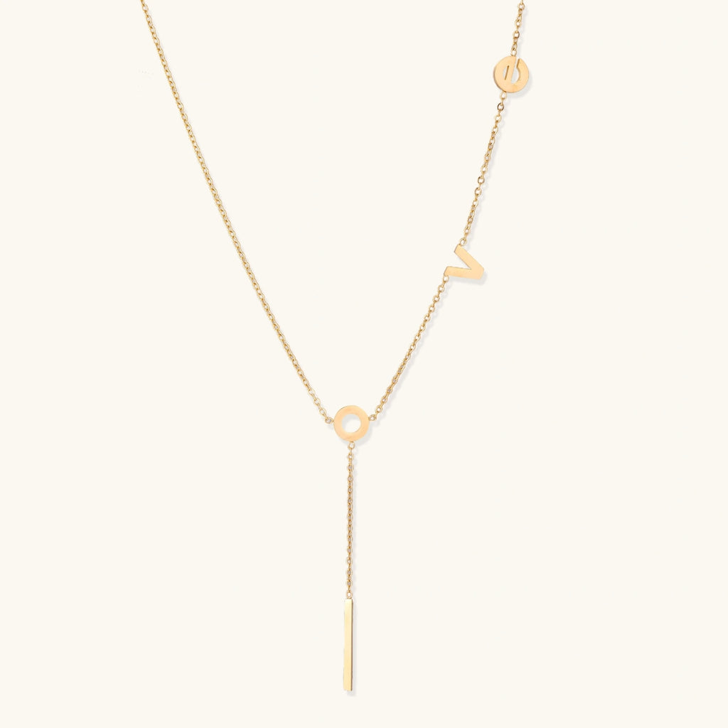 Gold Y-shaped necklace with L-O-V-E letter charms and vertical bar pendant on delicate chain against cream background