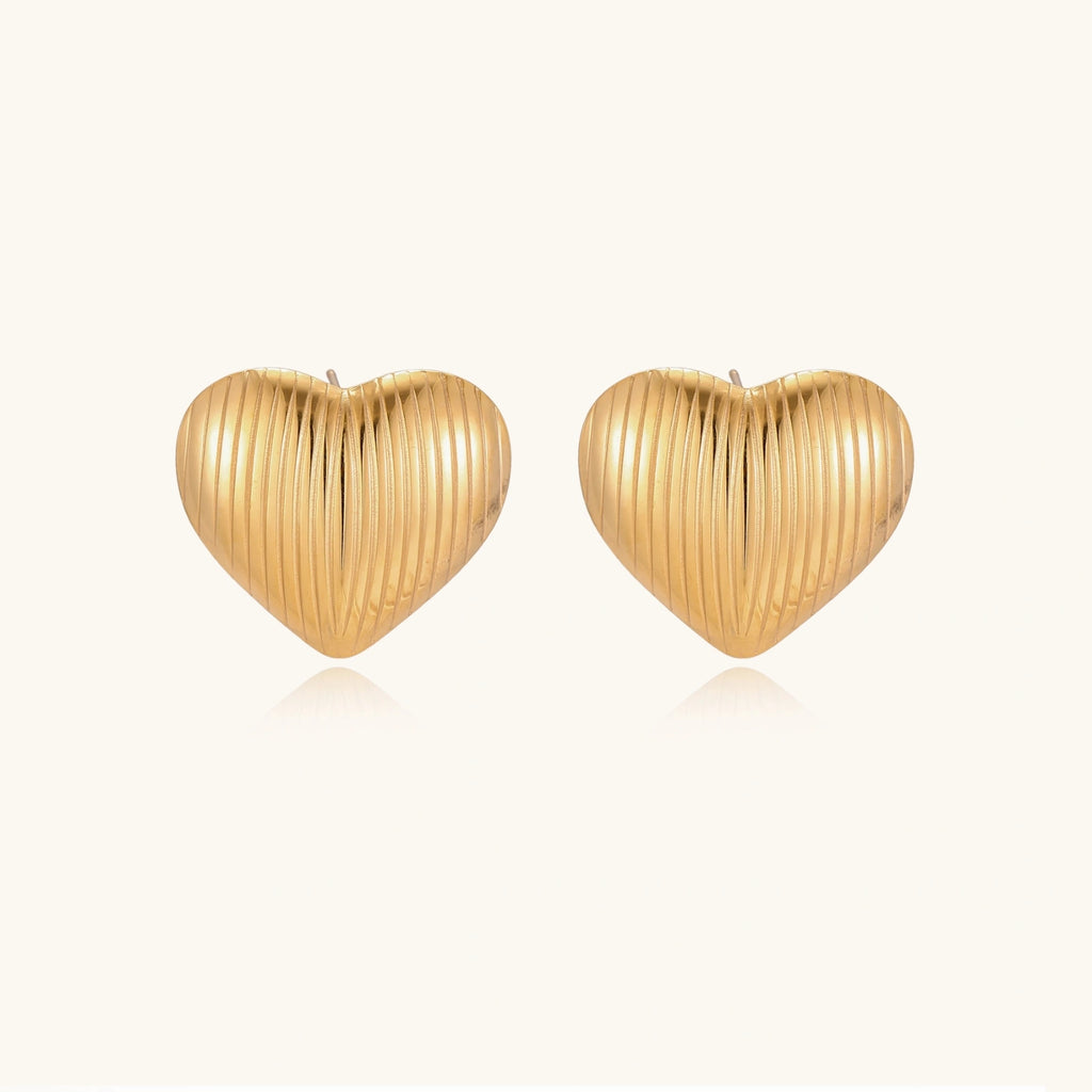 Gold heart-shaped stud earrings with parallel ridged texture on cream background
