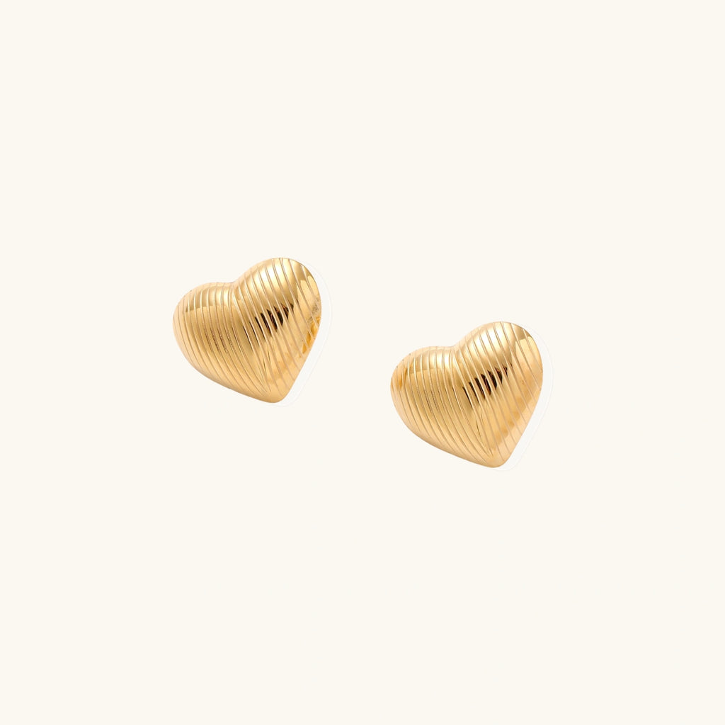 Gold heart-shaped stud earrings with parallel ridged texture on cream background