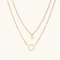 Gold layered necklace set with sunburst and smiley face pendants on delicate chains against white background.